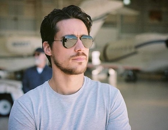 Peter Gadiot looking handsome in white t-shirt with black glasses.